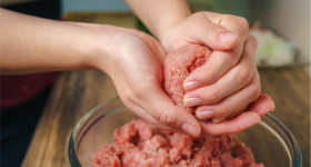 two hands mixing ground beef in a glass bowl